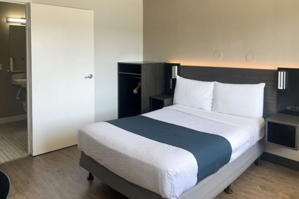 A hotel room with a bed, a nightstand, a wardrobe, and a door leading to a bathroom.