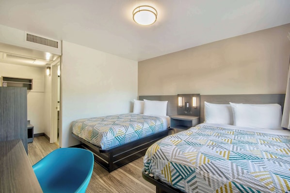 Una habitación de hotel con dos camas, una silla azul, un escritorio y un armario.