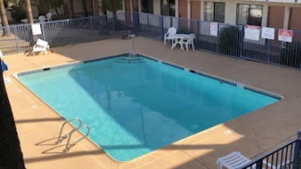 A rectangular swimming pool with a metal fence, surrounded by a multi-story building with balconies.