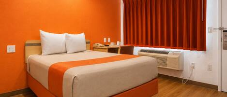 A hotel room with a bed, a desk with a telephone, and an air conditioning unit.