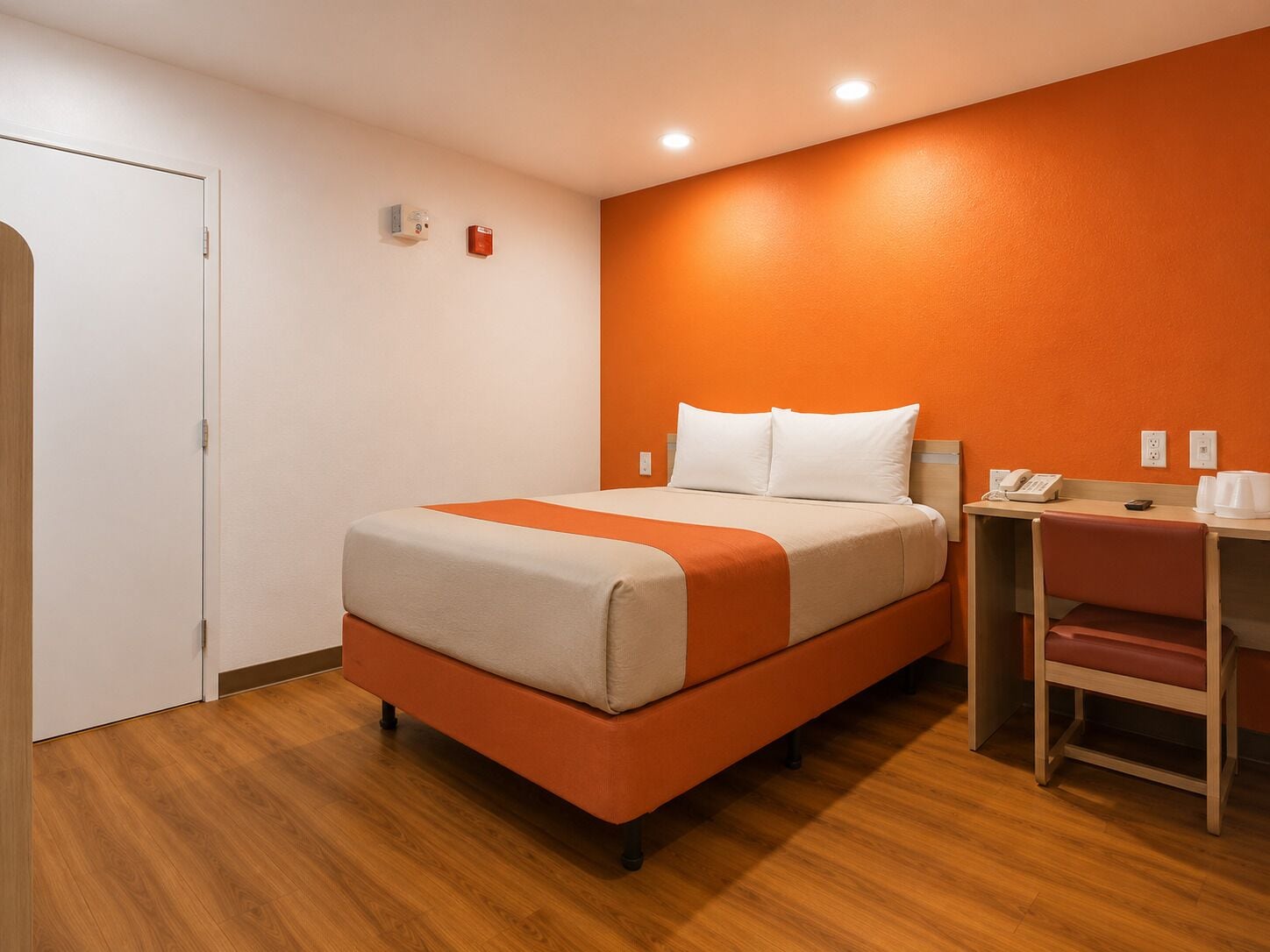 Una camera d'albergo con un letto, una scrivania con un telefono e tazze da caffè, e una sedia.