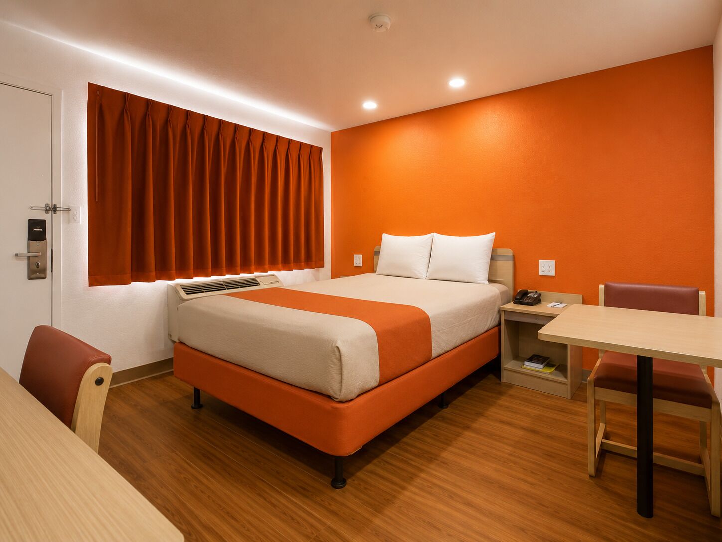 A hotel room with a bed, a desk, a chair, a window with curtains, and a door.