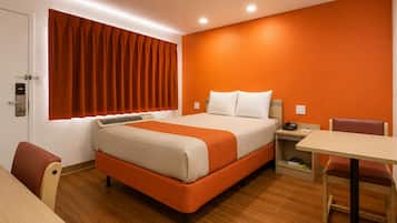 A hotel room with a bed, a desk, a chair, a window with curtains, and a door.
