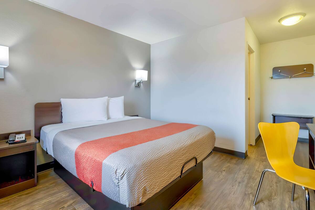 Una camera d'albergo con un letto, un comodino, una lampada e una scrivania con una sedia.