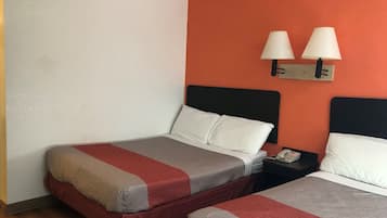 A hotel room with two beds, each with a red and grey bedspread, white pillows, and a black headboard. There are two bedside lamps on the wall, and a telephone on the nightstand.