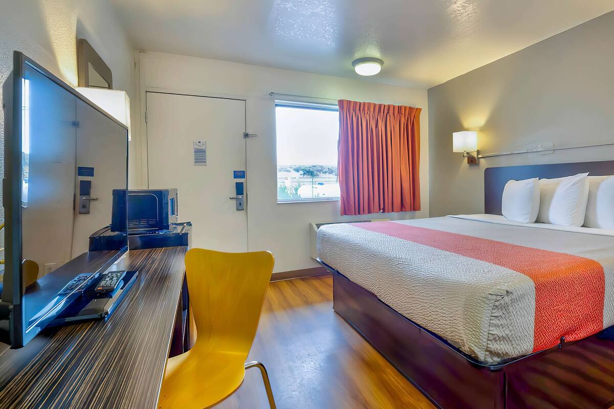 Una camera d'albergo con un letto, una scrivania con un computer, una sedia e una finestra con tende.