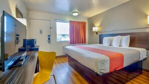 A hotel room with a bed, a desk with a computer, a chair, and a window with curtains.