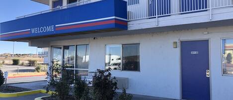 A hotel with a 'Welcome' sign, a blue door, and a registration window.