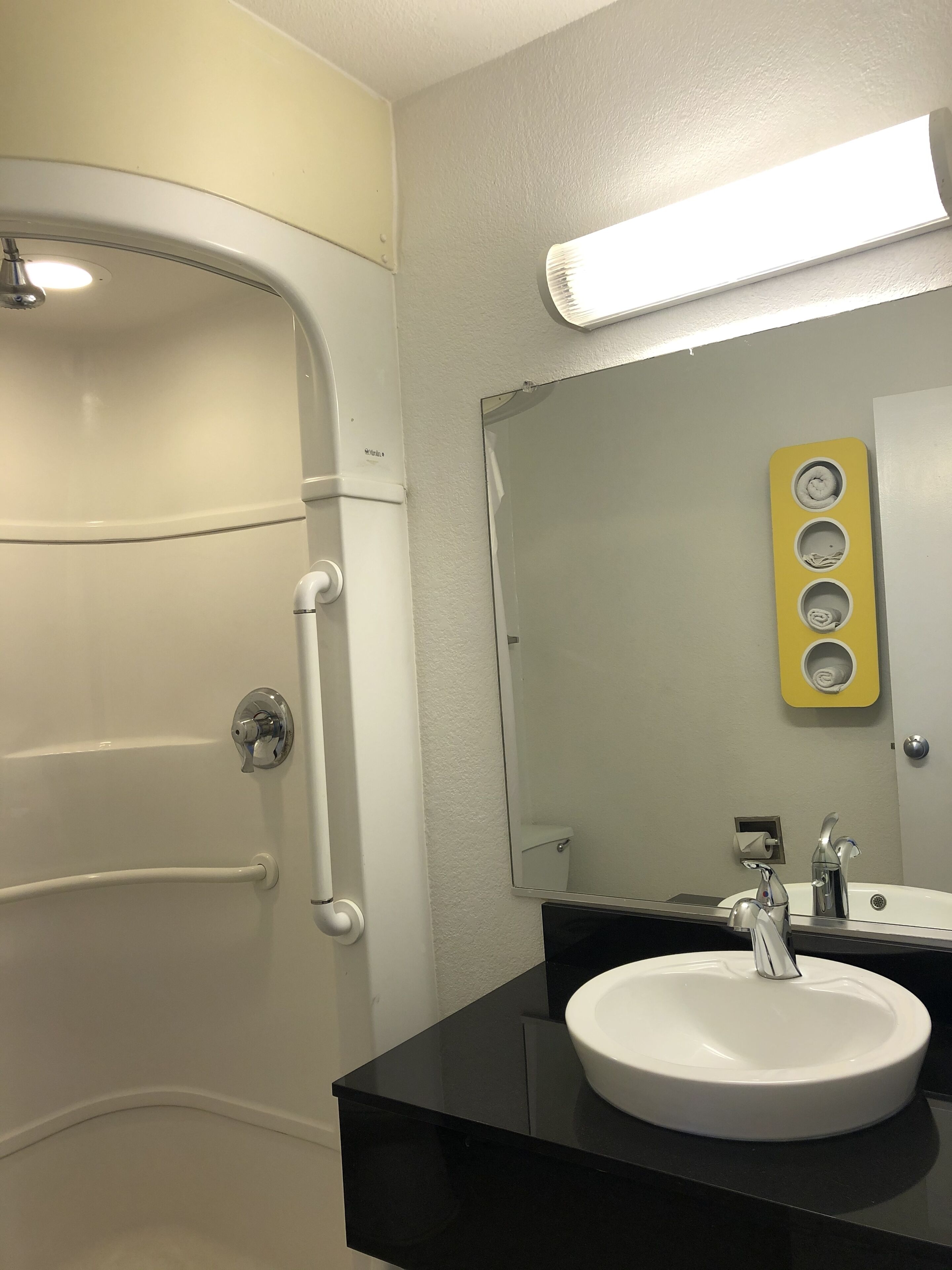 Un baño con una bañera blanca, un lavabo negro, un espejo y un jabonera amarilla.