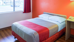 A hotel room with a bed, a window with a view of the street, and a red curtain.
