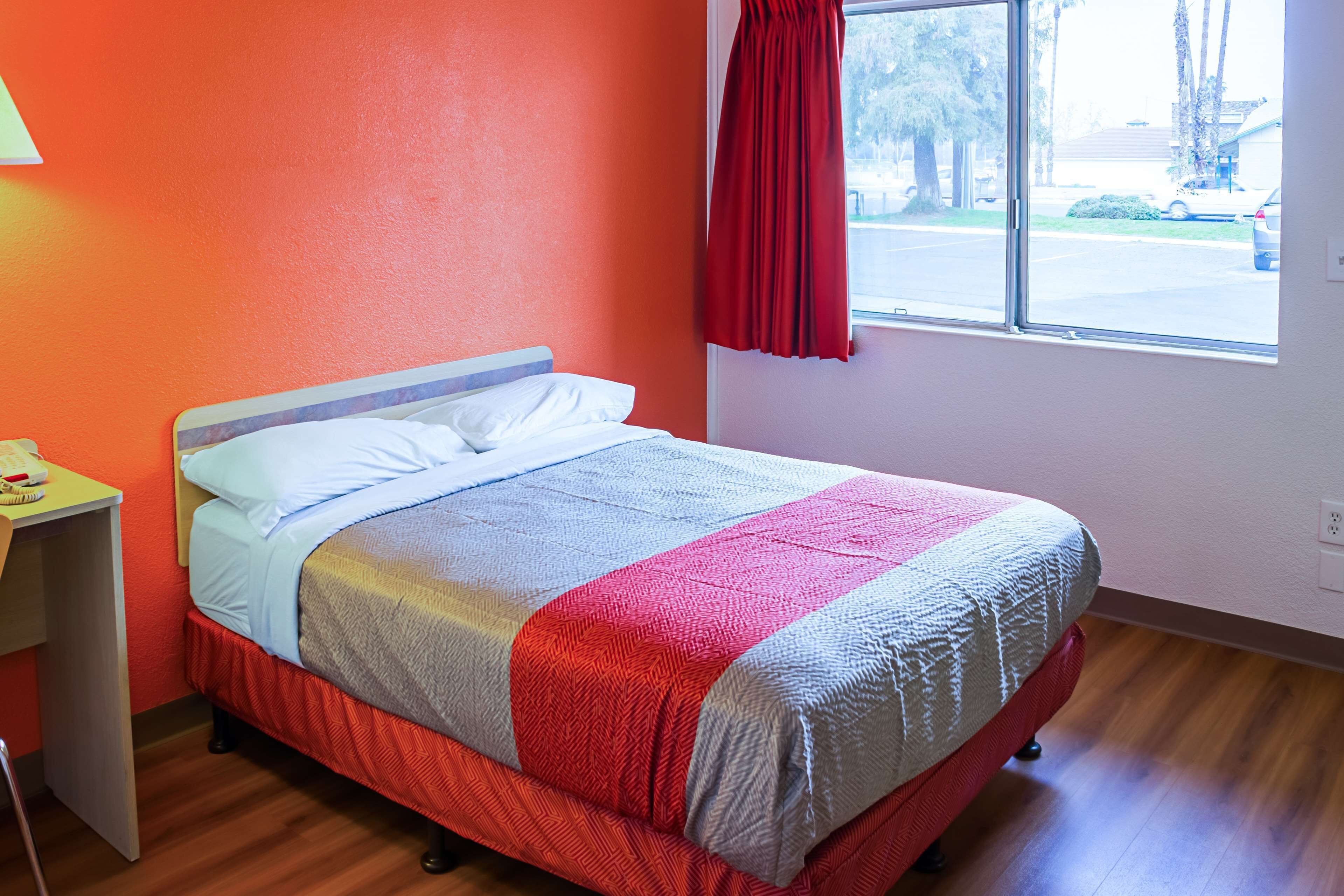 Un lit simple avec une couvre-lit rouge et blanc, un plancher en bois et une fenêtre avec un rideau rouge.