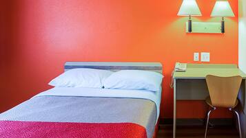 Habitación de hotel con cama, escritorio y silla. Hay dos lámparas de pared sobre el escritorio.