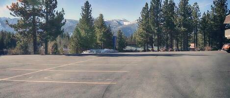 A parking lot with marked spaces, surrounded by trees and mountains in the background.