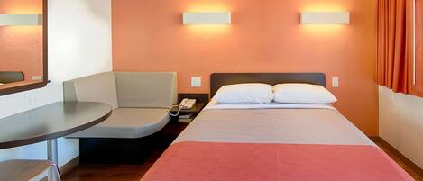 Habitación de hotel con cama, escritorio, una silla y dos lámparas de pared.