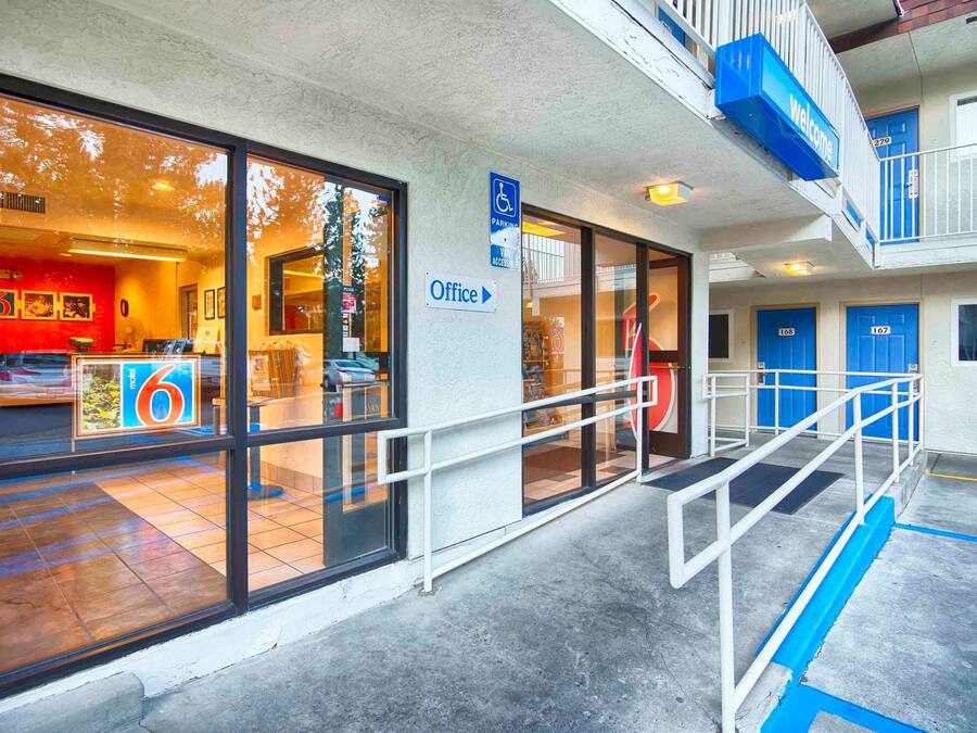 A hotel entrance with a reception area, marked parking sign, and a staircase leading to an upper level.