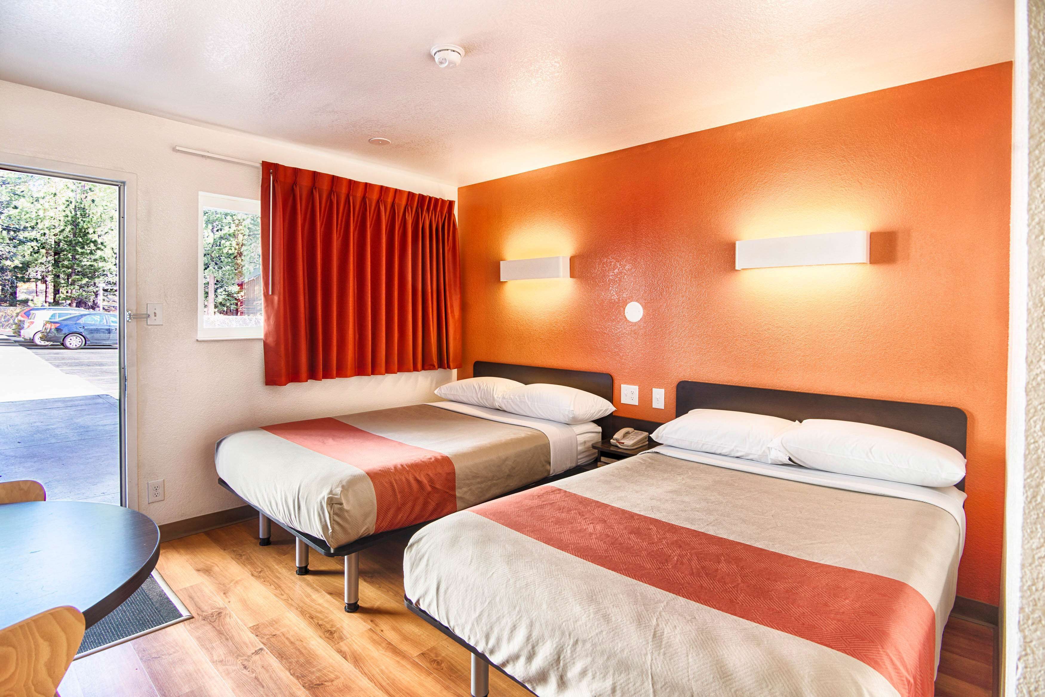 A hotel room with two beds, a dining table, and a window with curtains.