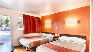 A hotel room with two beds, a dining table, and a window with curtains.