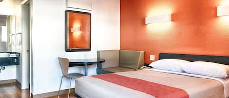 A hotel room with a bed, a desk, a chair, and a mirror.