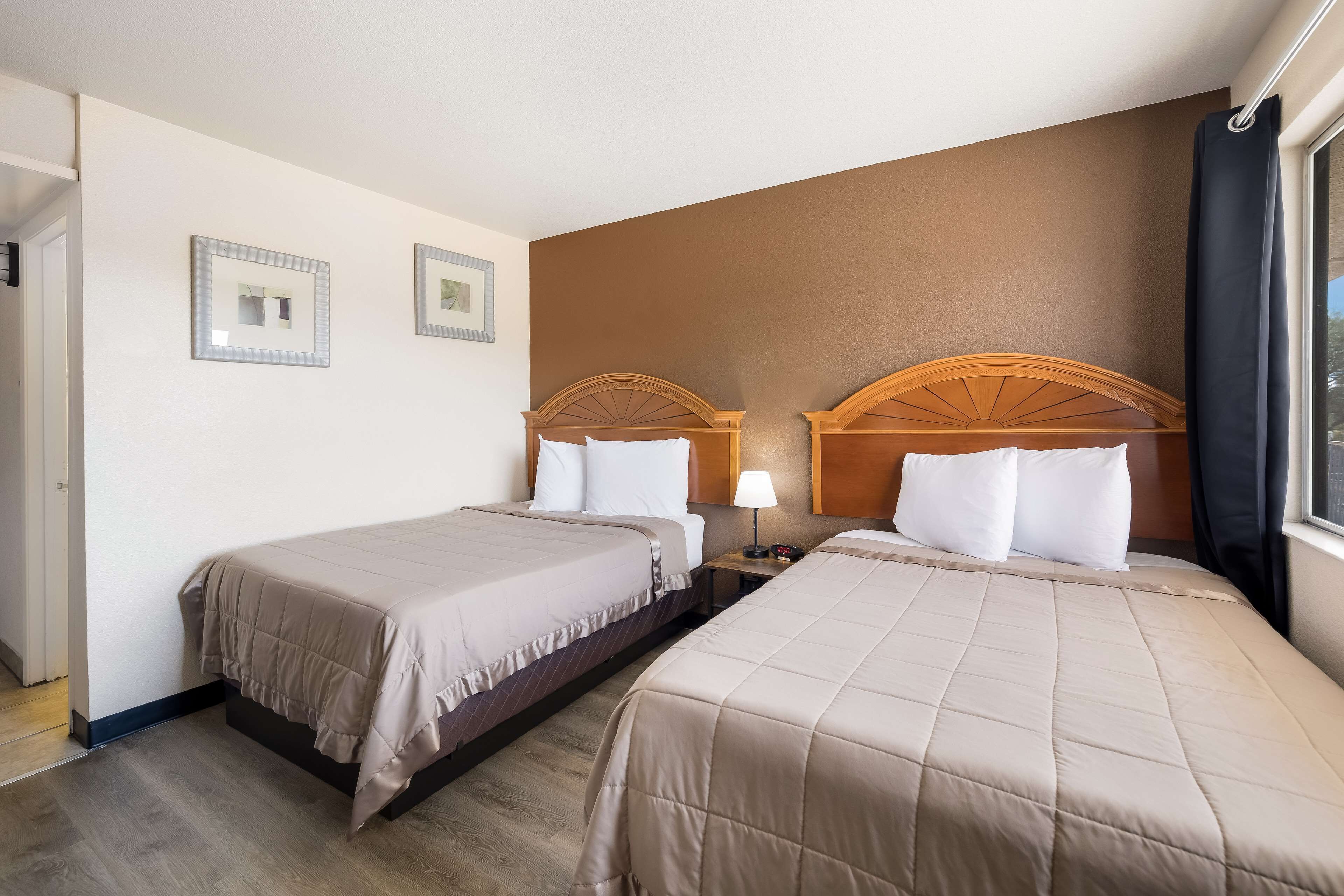 A hotel room with two beds, a nightstand with a lamp, and a window with curtains.