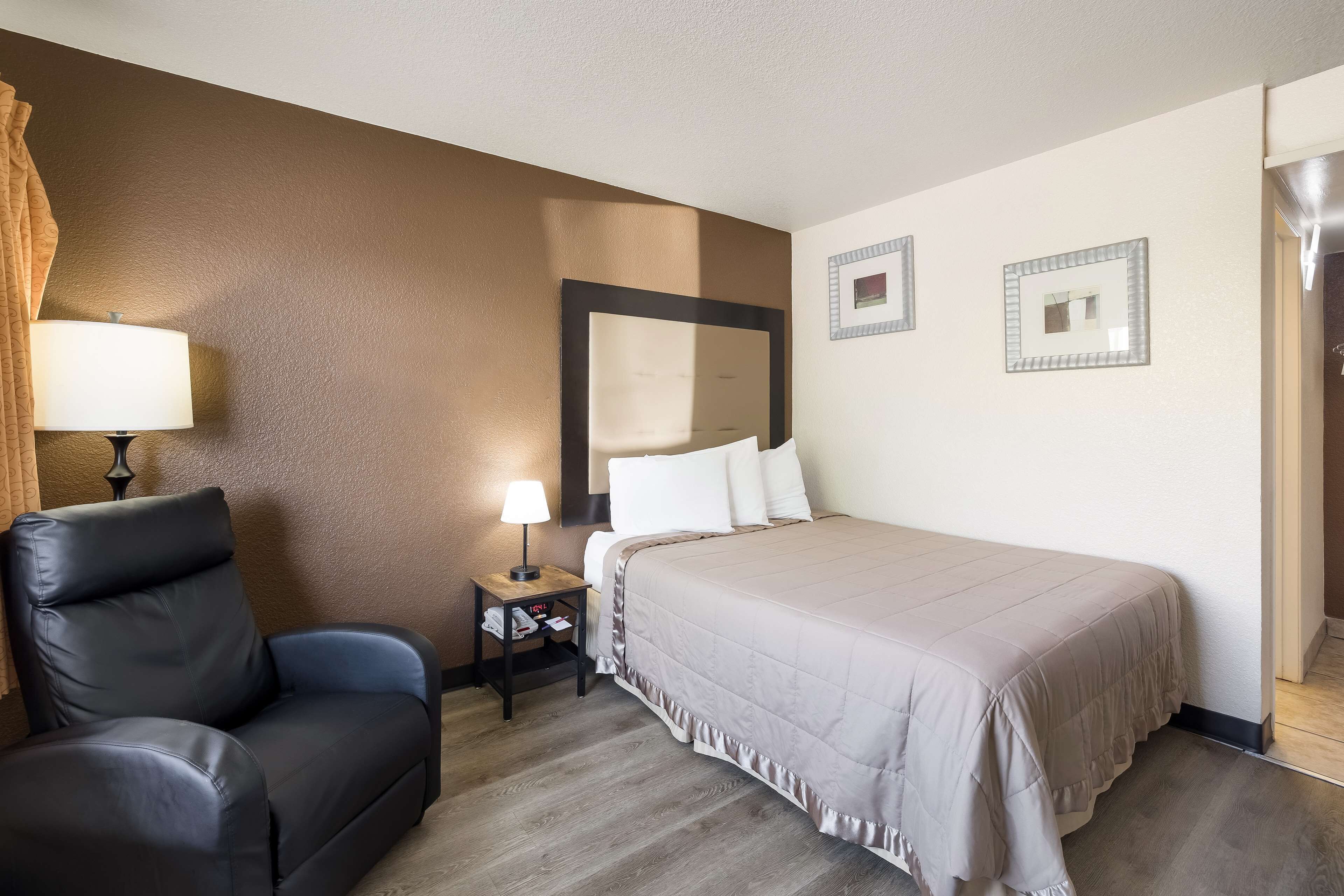 A hotel room with a bed, a chair, a nightstand, and a lamp.