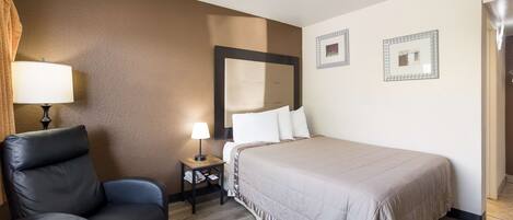 A hotel room with a bed, a chair, a nightstand, and a lamp.