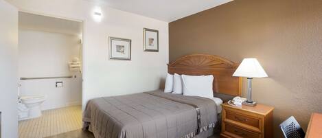A neatly arranged hotel room with a bed, bedside table, and a bathroom visible through an open door.