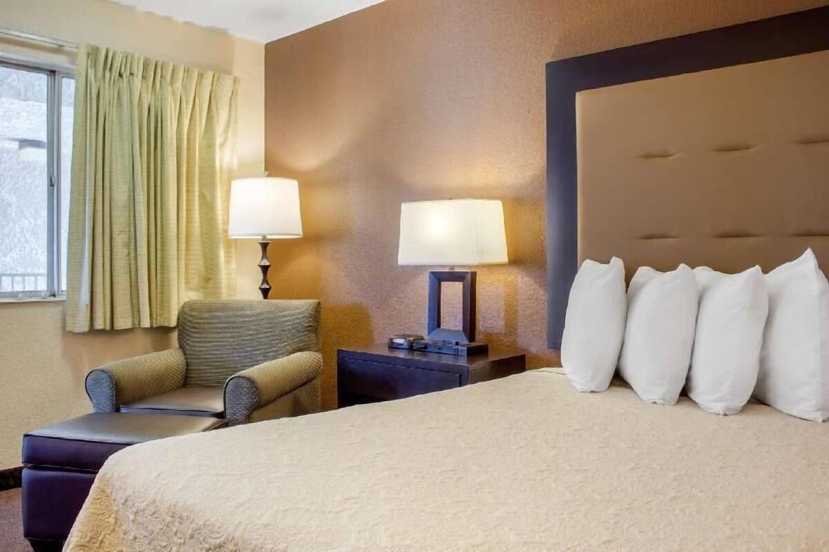 Une chambre d’hôtel avec un lit, deux lampes de chevet, une chaise, une table de chevet et une fenêtre avec des rideaux.