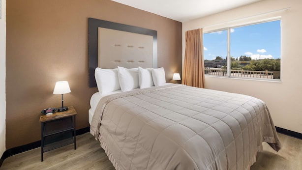 Habitación de hotel con una cama grande, una mesita de noche con lámpara y una ventana con vistas al exterior.