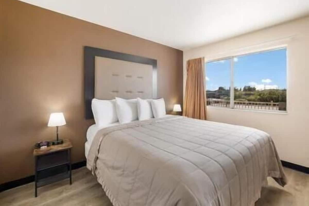 Une chambre d’hôtel avec un grand lit, une table de chevet, une lampe et une fenêtre donnant sur un beau paysage.