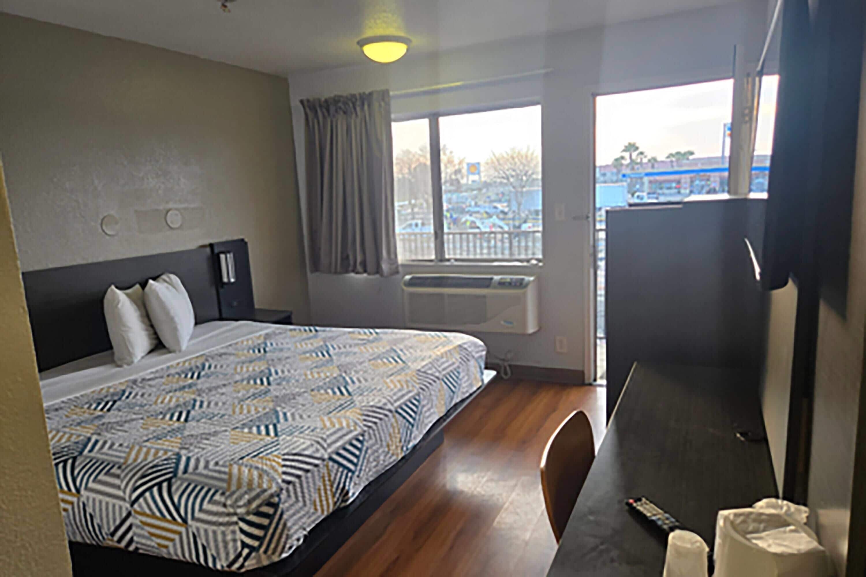 A hotel room with a bed, a desk, a window, and a view of a parking lot.