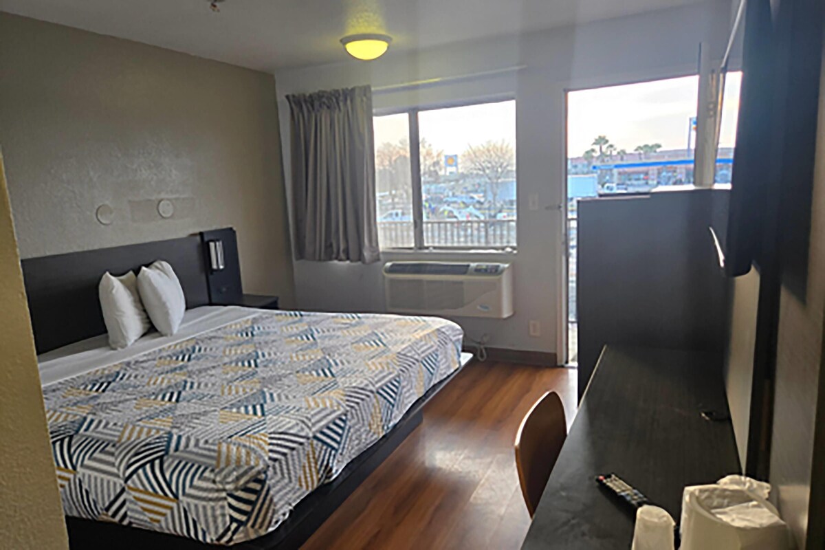 A hotel room with a bed, a desk, a window, and a view of a parking lot.