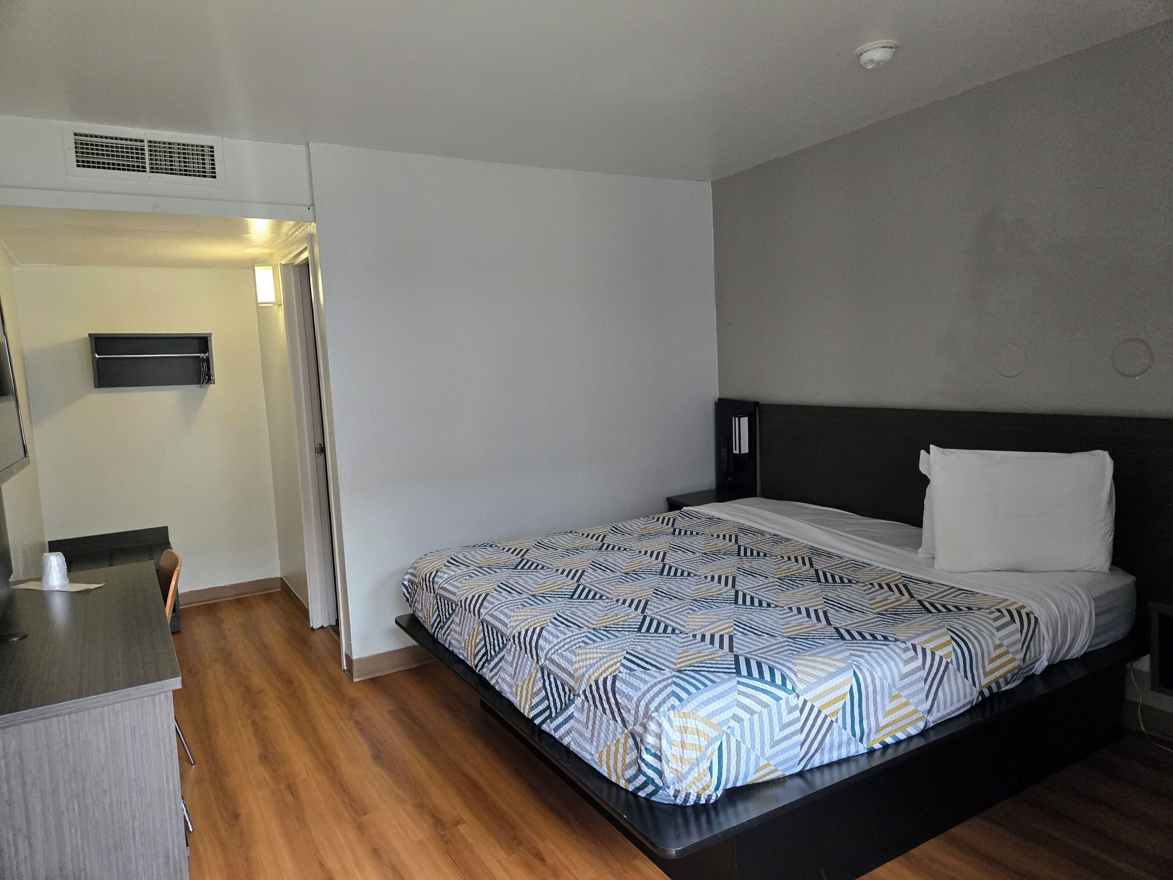 A modern hotel room with a bed, bedside table, and a small desk.