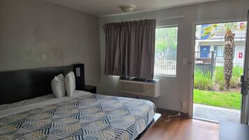 A hotel room with a bed, a window with curtains, an air conditioning unit, and a view of the outside.