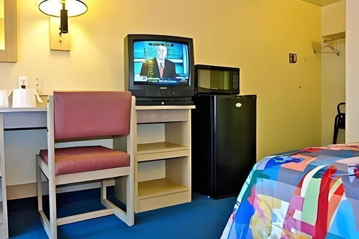 Ein Hotelzimmer mit Fernseher auf einem Tisch, einem kleinen Kühlschrank, einem Etagenbett mit rotem Kissen und einer bunten Steppdecke auf dem Bett.