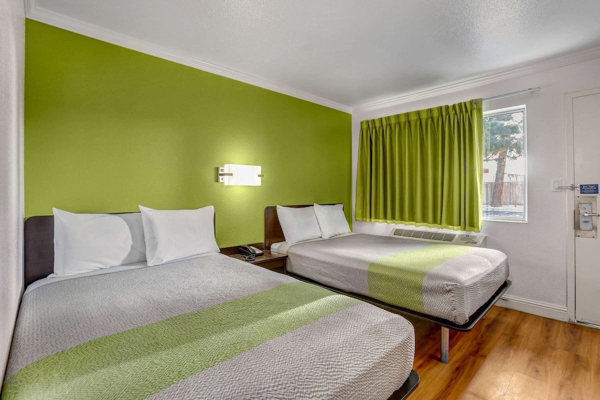 Ein Hotelzimmer mit zwei Betten, einer grünen Wand, einem Fenster mit Vorhängen und einer Tür.