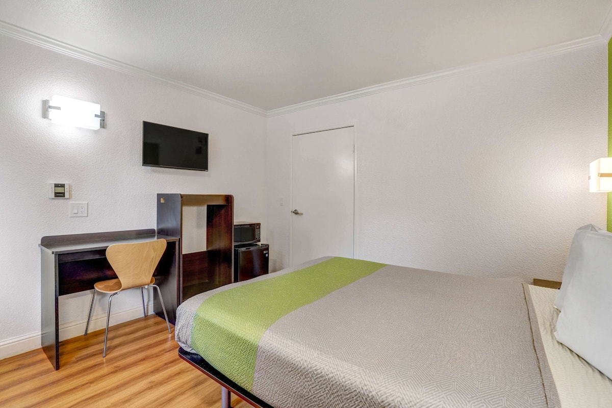 Ein Hotelzimmer mit einem Bett, einem Schreibtisch mit Stuhl, einem Fernseher und einer Tür.