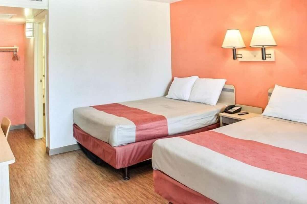 Ein Hotelzimmer mit zwei Betten, einem Nachttisch mit Lampe und einer Tür zu einem anderen Raum.