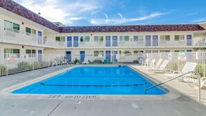 A swimming pool with a 3ft no diving sign, surrounded by lounge chairs and a multi-story building with balconies.