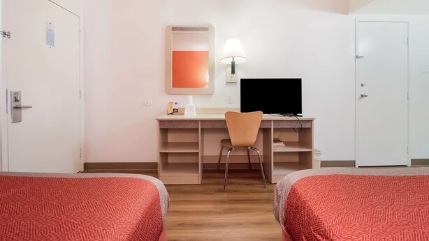 A hotel room with two beds, a desk with a chair, a TV, and a lamp.