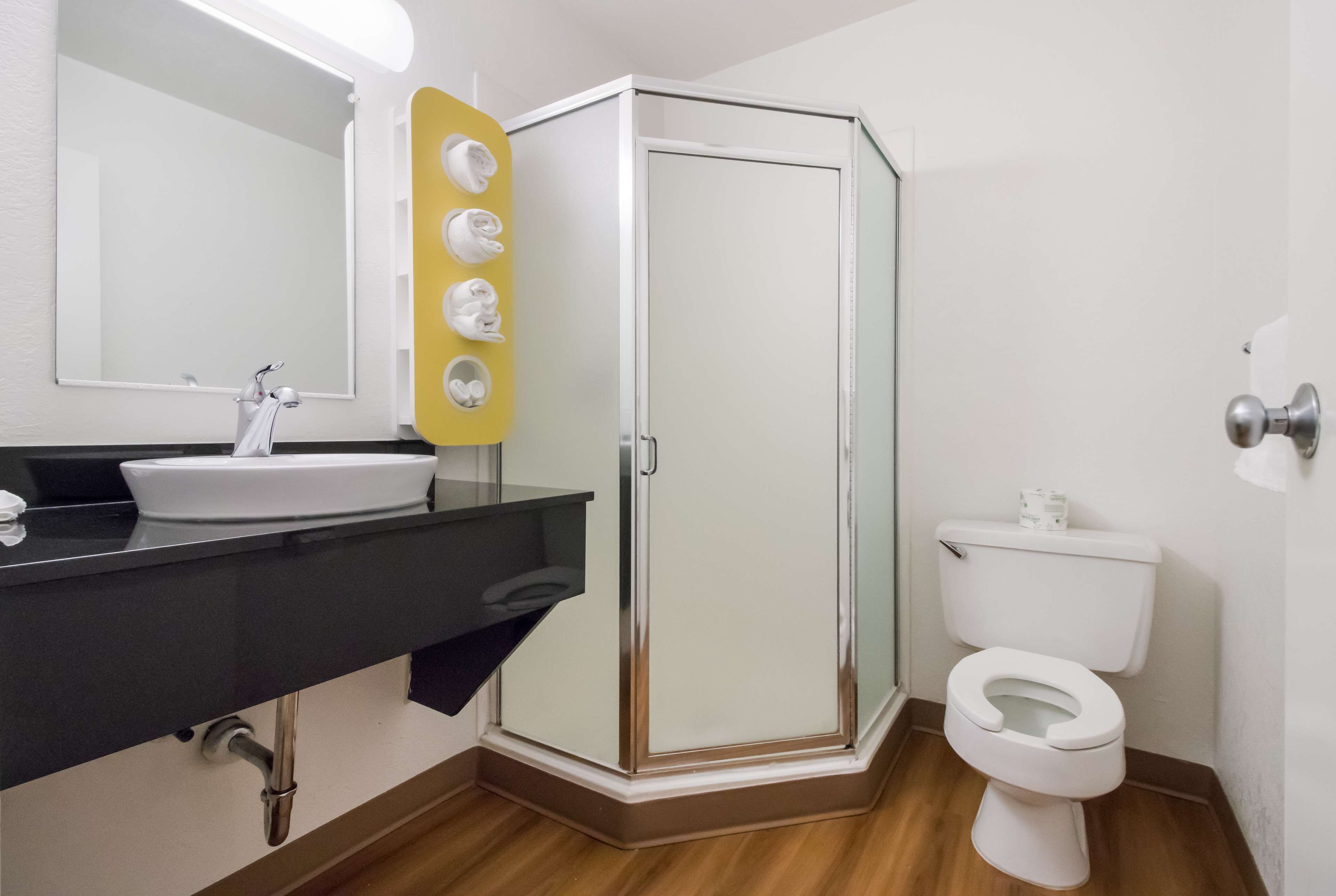 A bathroom with a white sink, mirror, and toilet. There is a shower with a glass door and a yellow towel rack.