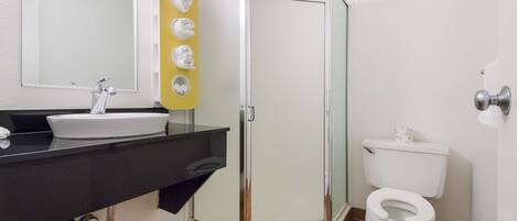 A bathroom with a white sink, mirror, and toilet. There is a shower with a glass door and a yellow towel rack.