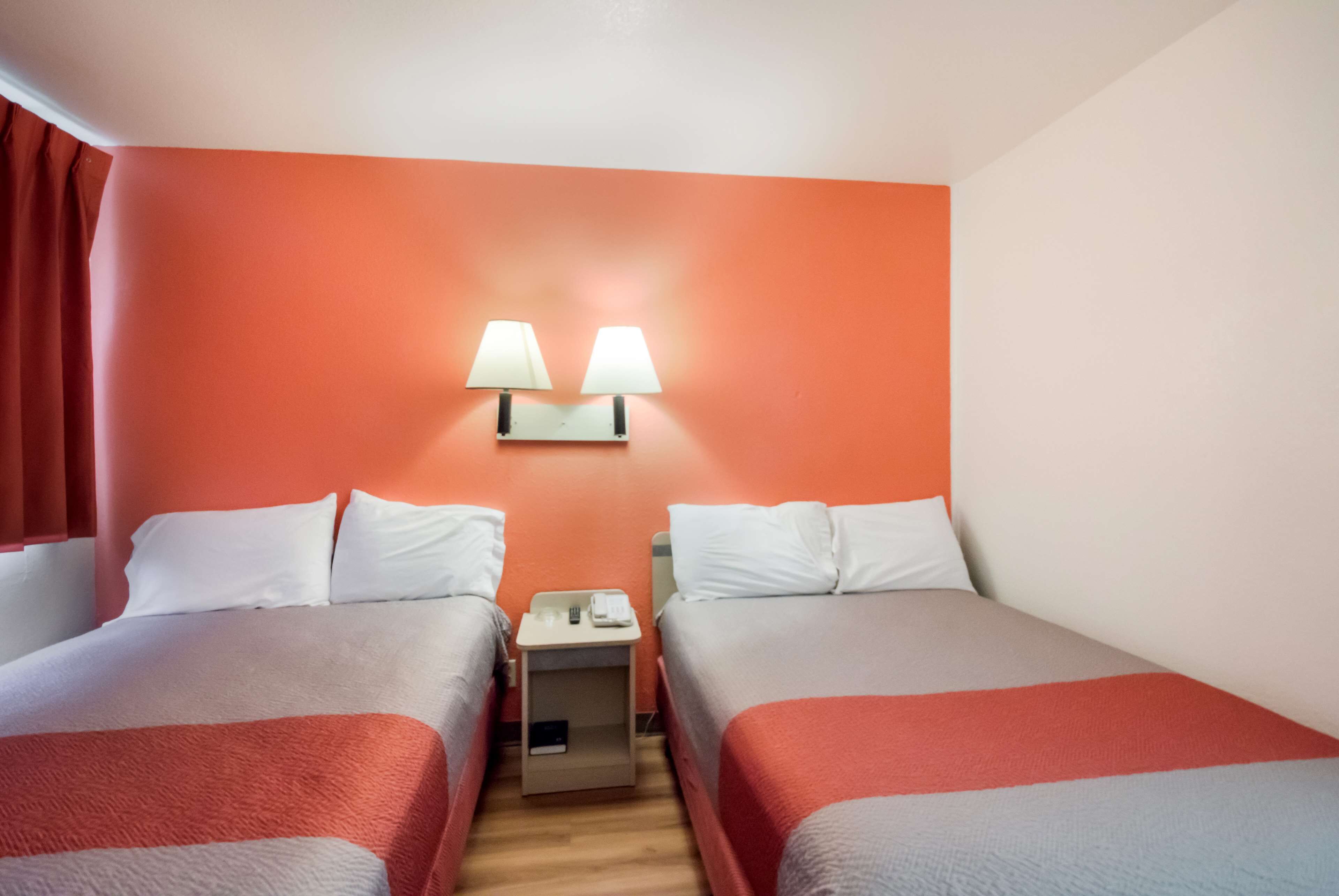 Habitación de hotel con dos camas, una mesita de noche y dos lámparas de pared.