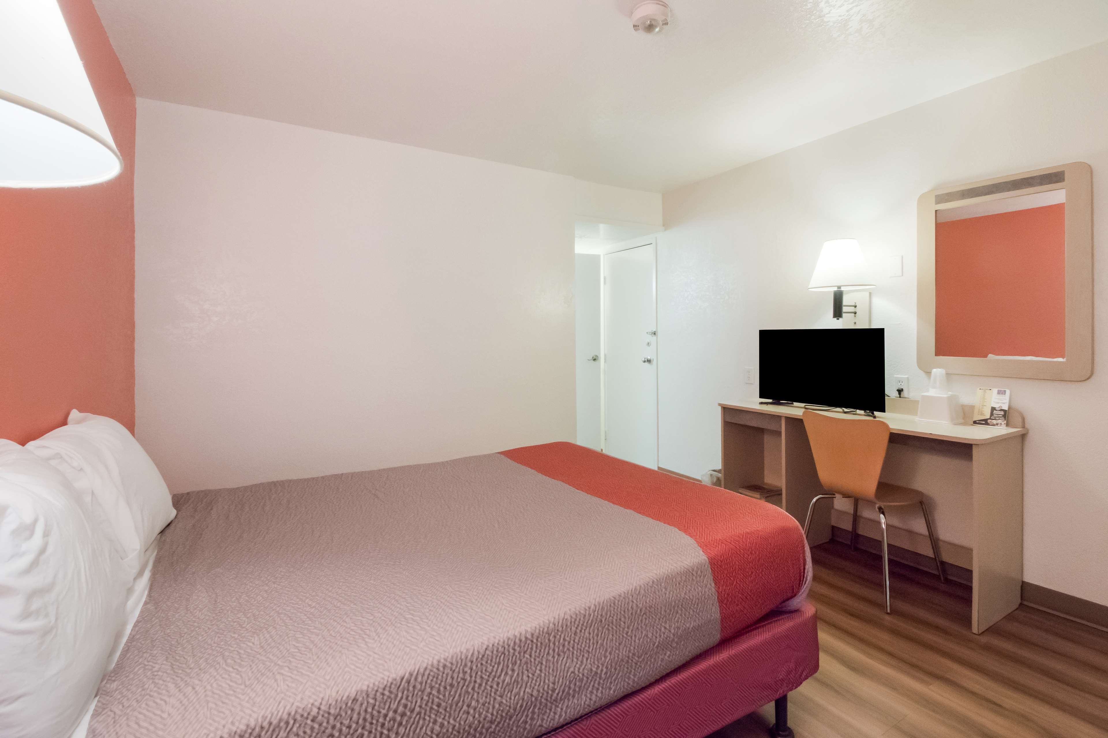 Una habitación de hotel con una cama, un escritorio con computadora, una silla, una lámpara y un espejo.