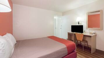 Una habitación de hotel con una cama, un escritorio con computadora, una silla, una lámpara y un espejo.