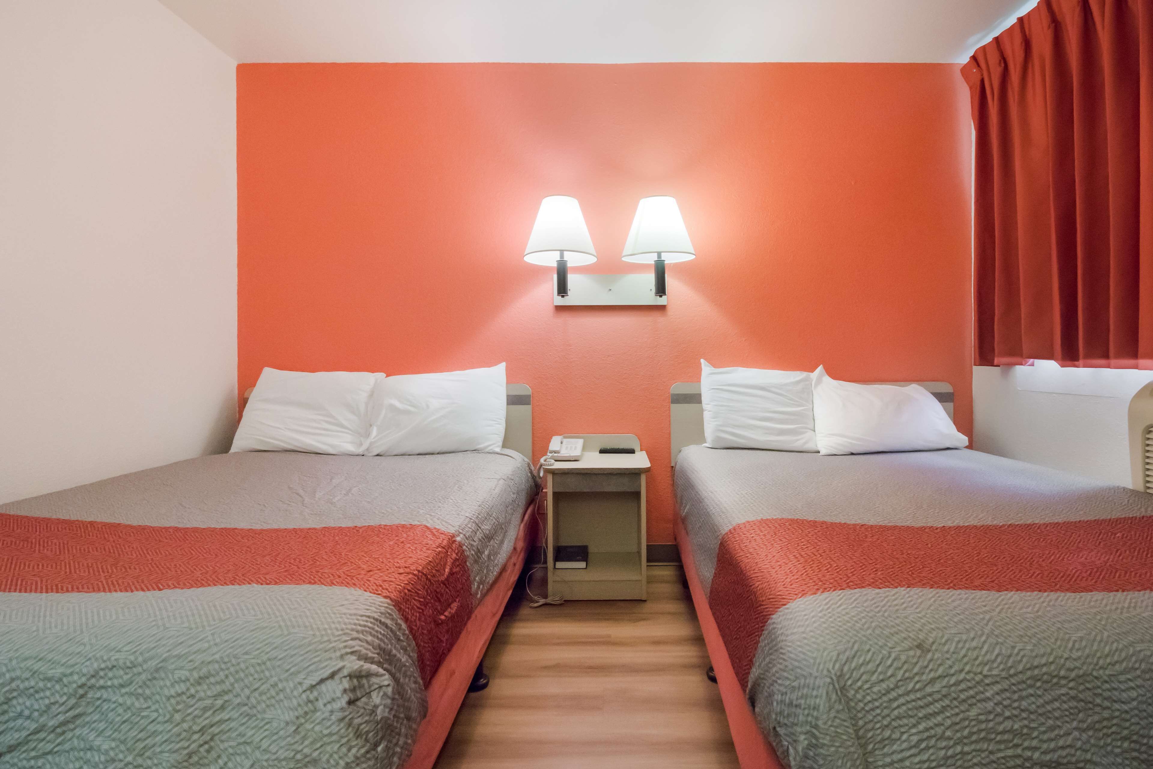 Et hotelværelse med to senge, et natbord med telefon og en lampe monteret på væggen.