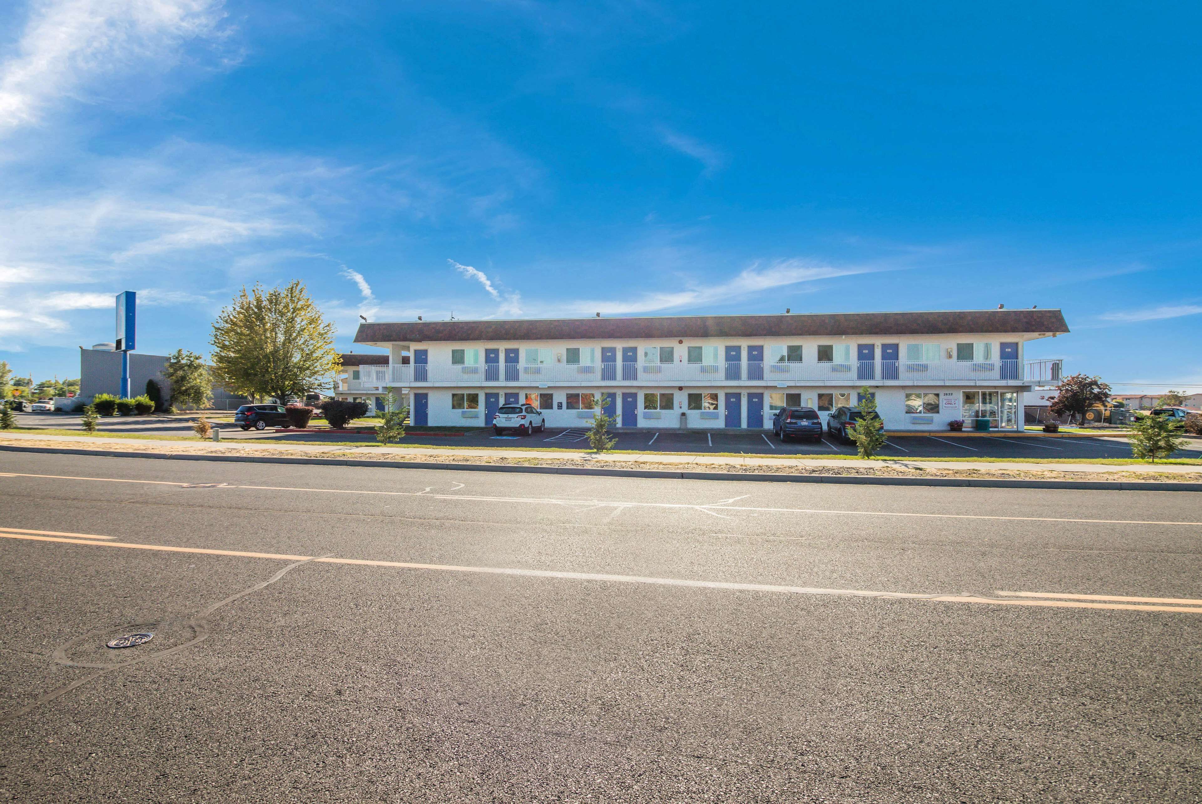 A motel with a row of rooms, a parking lot, and a clear blue sky.