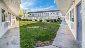 A motel with a covered walkway, a grassy courtyard, and a row of rooms with windows.