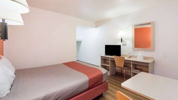 A hotel room with a bed, desk, chair, and a television.