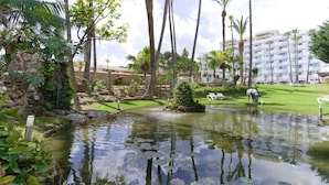 A serene pond with a small island, surrounded by lush greenery and tall palm trees. - BLUESEA Al Andalus (Torremolinos)