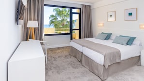 A hotel room with a bed, a desk, and a view of palm trees and the sea. - BLUESEA Al Andalus (Torremolinos)